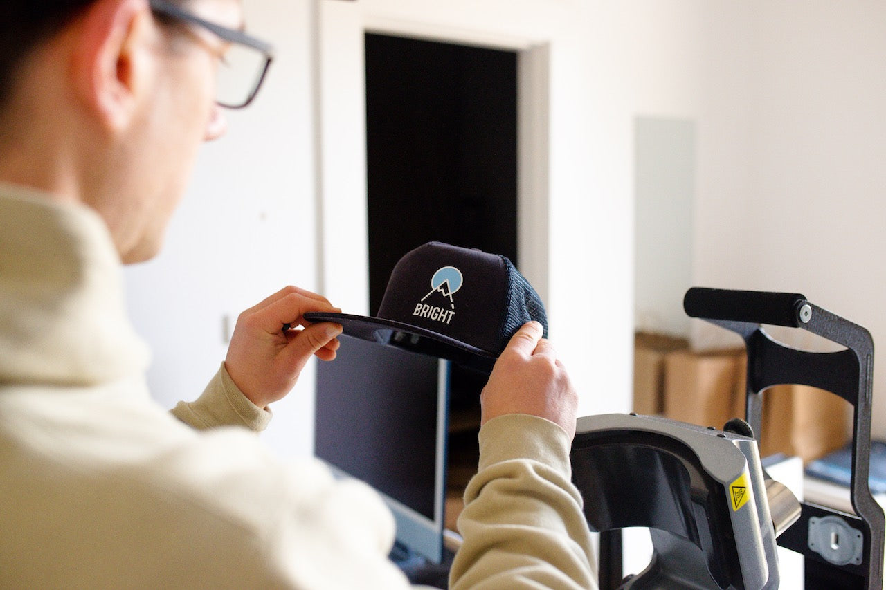 Person holding a cap with a logo in front of a computer screen